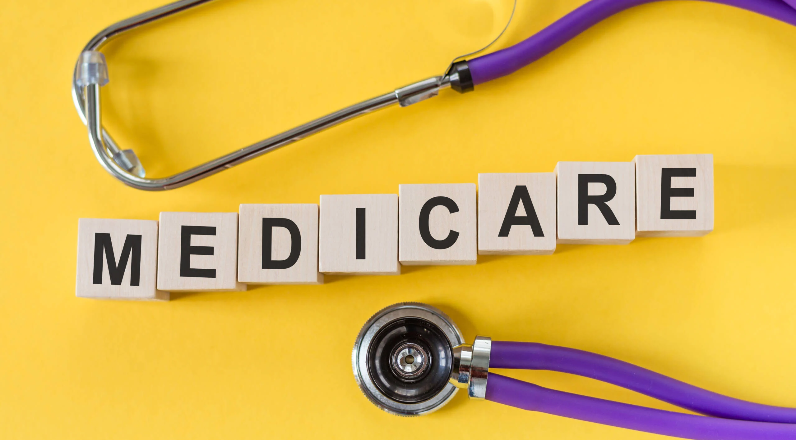 Medicare written on cube shape wooden blocks set on a yellow table with a stethoscope.