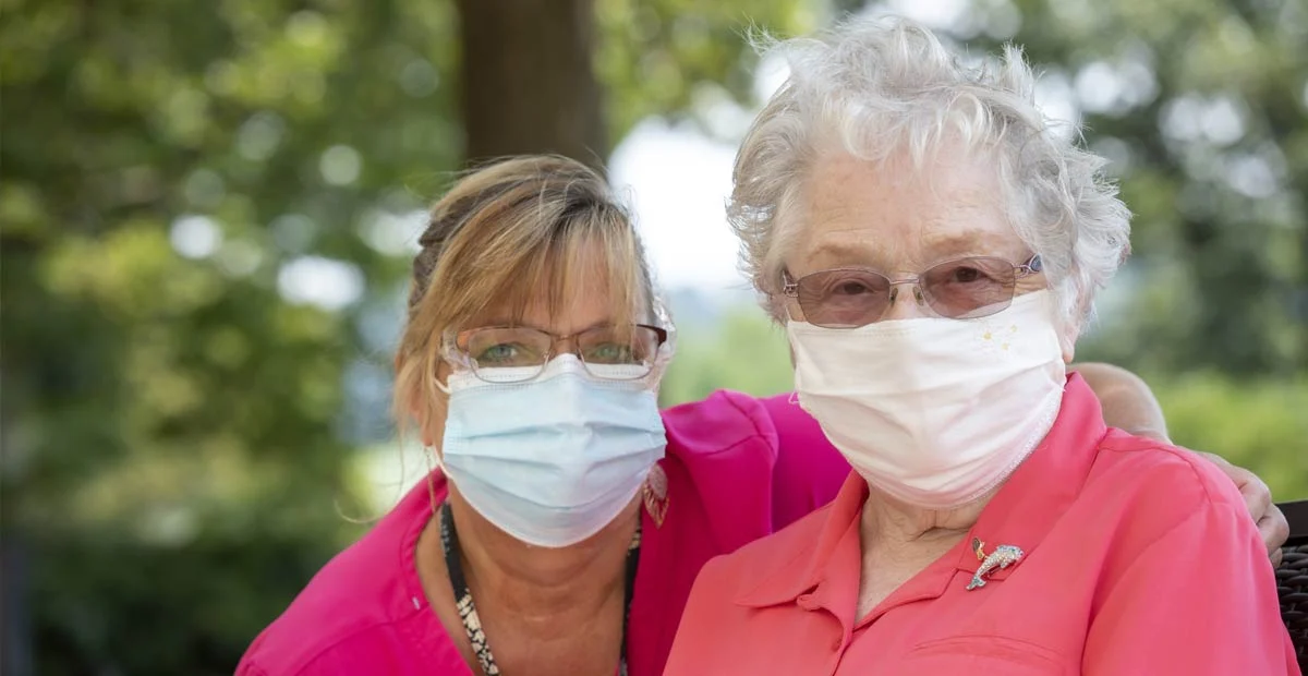 Nurse and long term care resident wearing masks while seated outdoors.