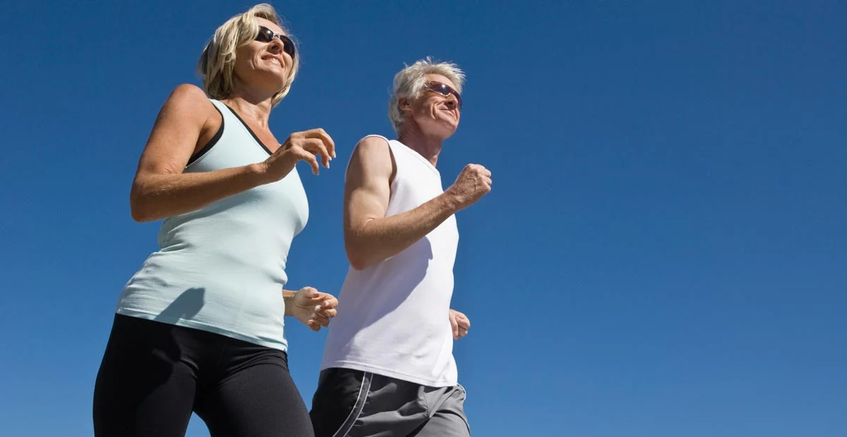 Senior couple running together outdoors with a clear blue sky behind them.