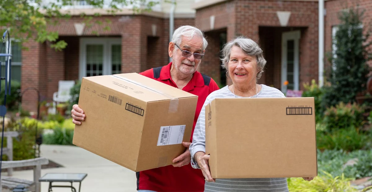 Smiling Senior couple holding moving boxes while standing in a courtyard.