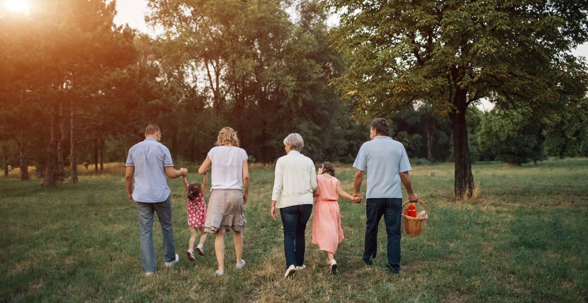 Intergenerational group walking outdoors, one man is holding a picnic basket.