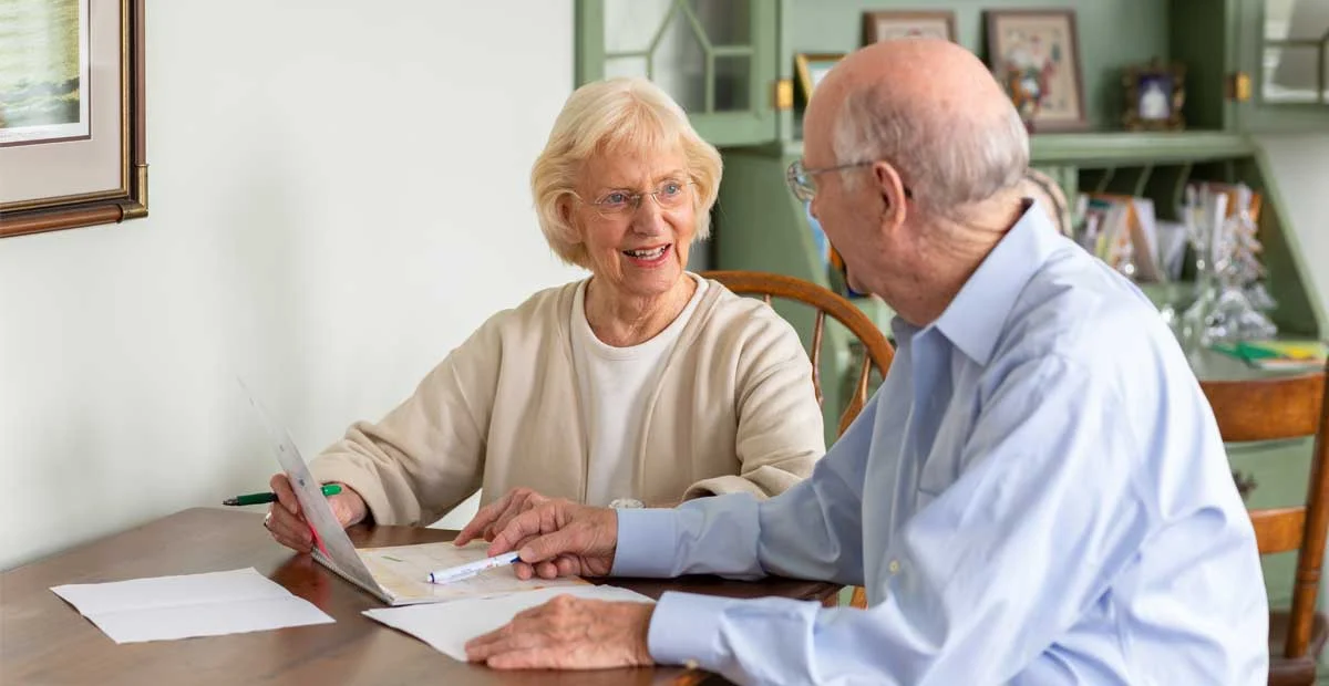 Smiling senior couple seated at kitchen table going over paperwork together.