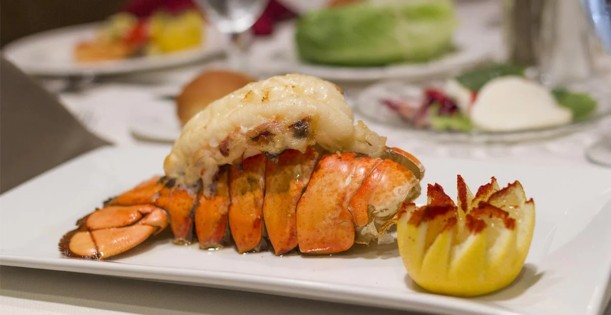 Gourmet lobster tail with seared lemon next to it on a white plate.