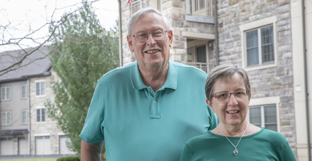 Smiling senior couple standing in front of stone apartment building.