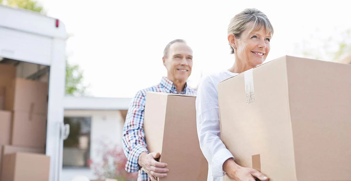 Senior couple carrying boxes from a moving truck outdoors.