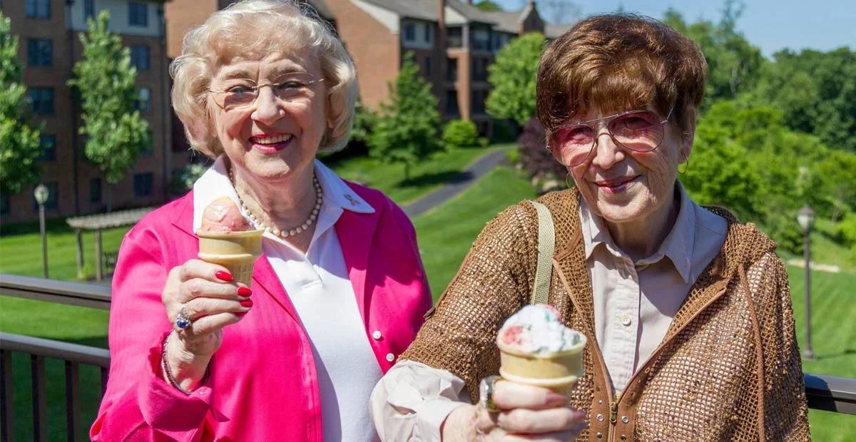 Smiling senior women raising up ice cream cones while standing outside.