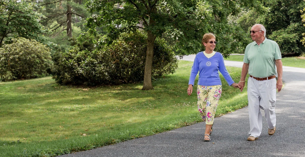 Older couple walking while holding hands outdoors.