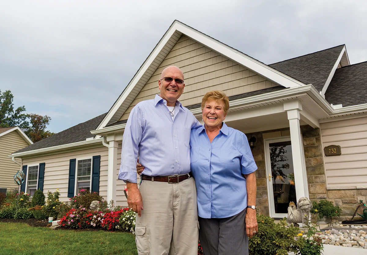 Smiling senior couple standing in front of cottage.