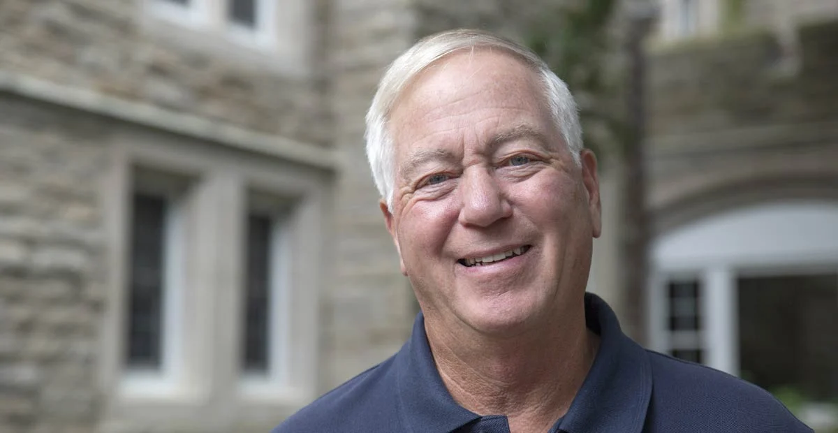 Smiling senior man standing in front of a stone building.