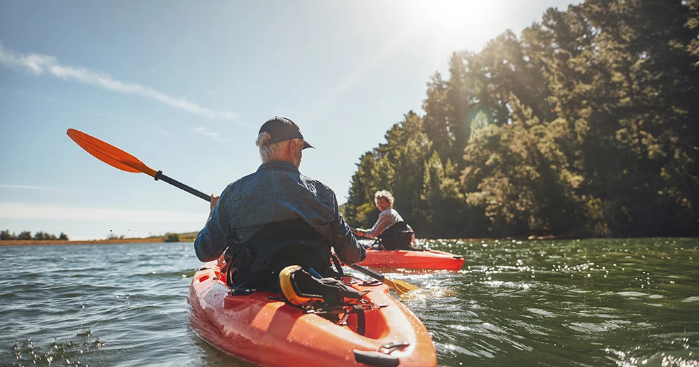 Couple kayaking on tree-lined lake together.