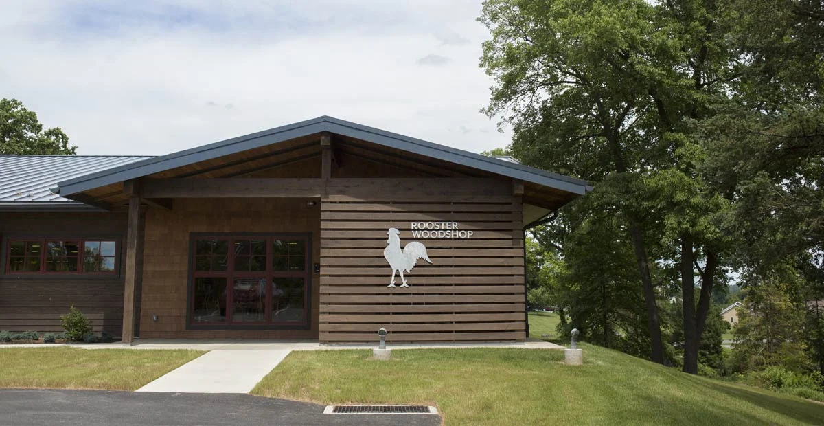 A one-story, building with wood exterior with sign reading, "Rooster Woodshop."