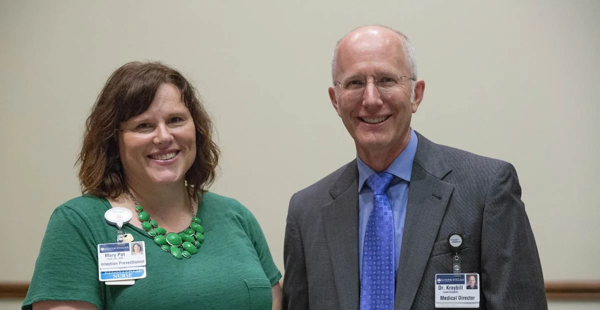 Smiling woman and man wearing name tags standing next to one another indoors.