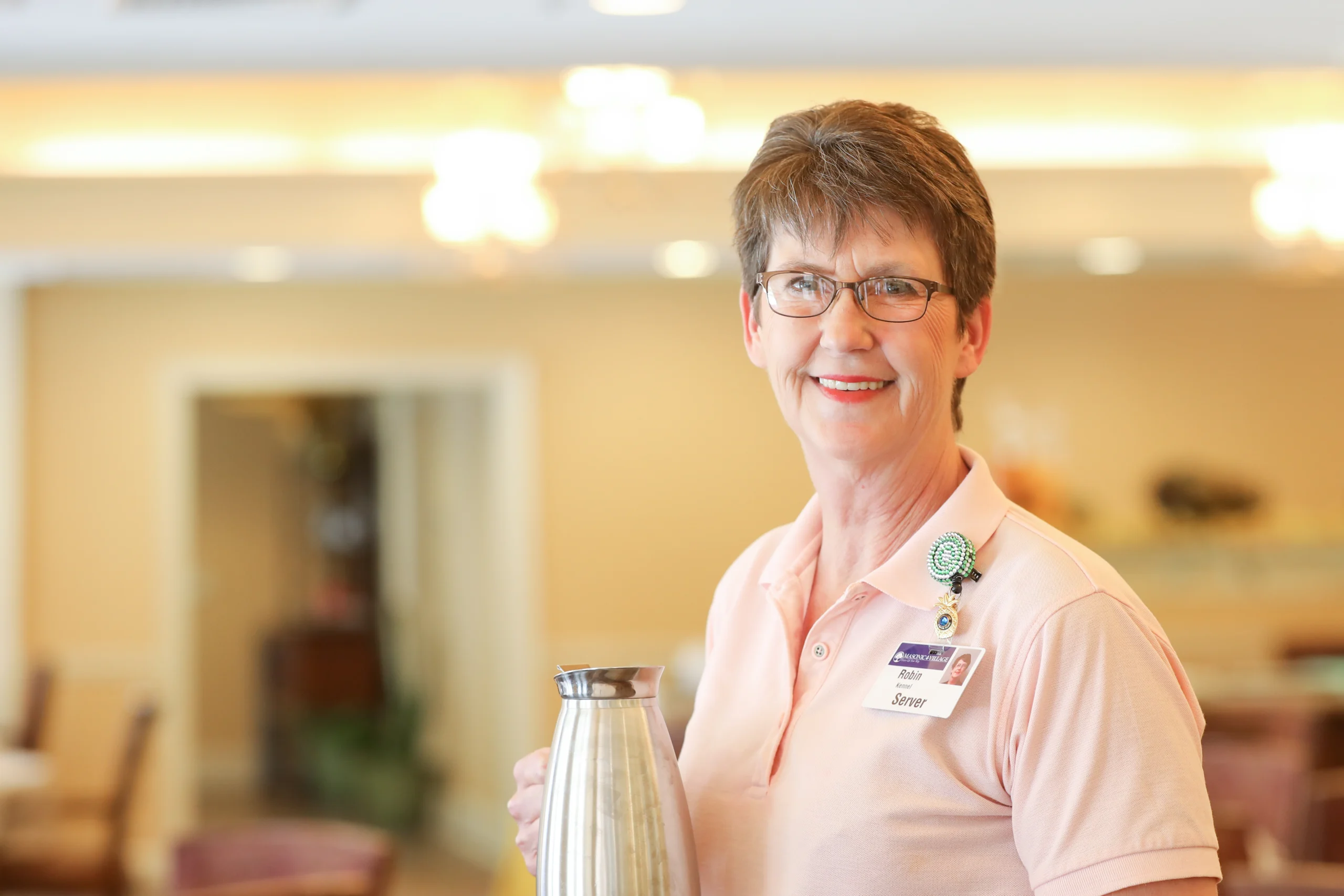 Smiling woman holding a carafe while standing in dining room at Masonic Village. at Elizabethtown