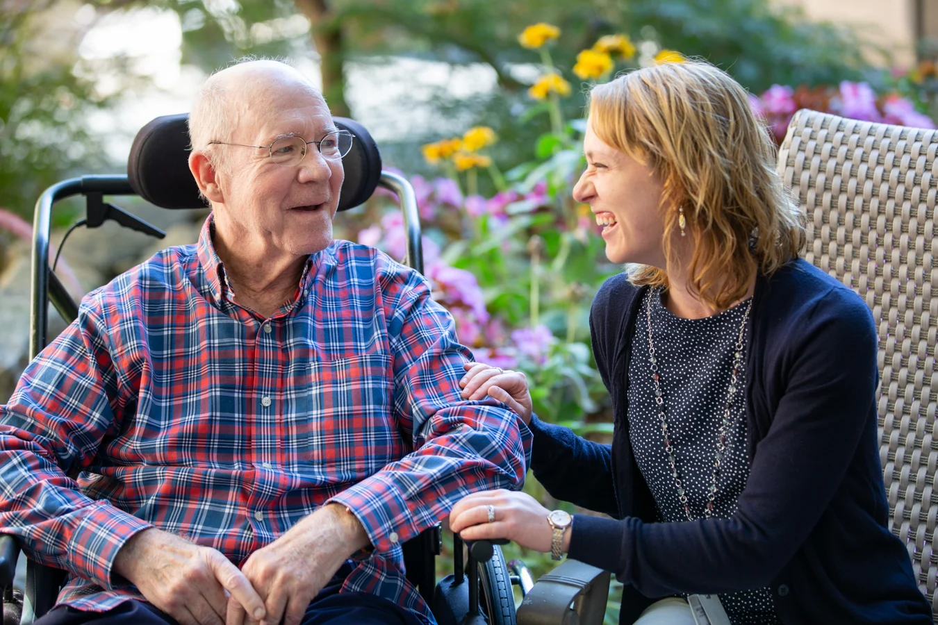Smiling senior man and nurse seated together outdoors in garden.