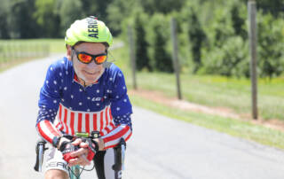 Smiling senior man wearing a helmet and biking outfit while riding his bicycle outdoors.
