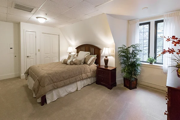 Neutral-toned bedroom with beige carpet, and deep wood furniture, including a bed, night stand and dresser.