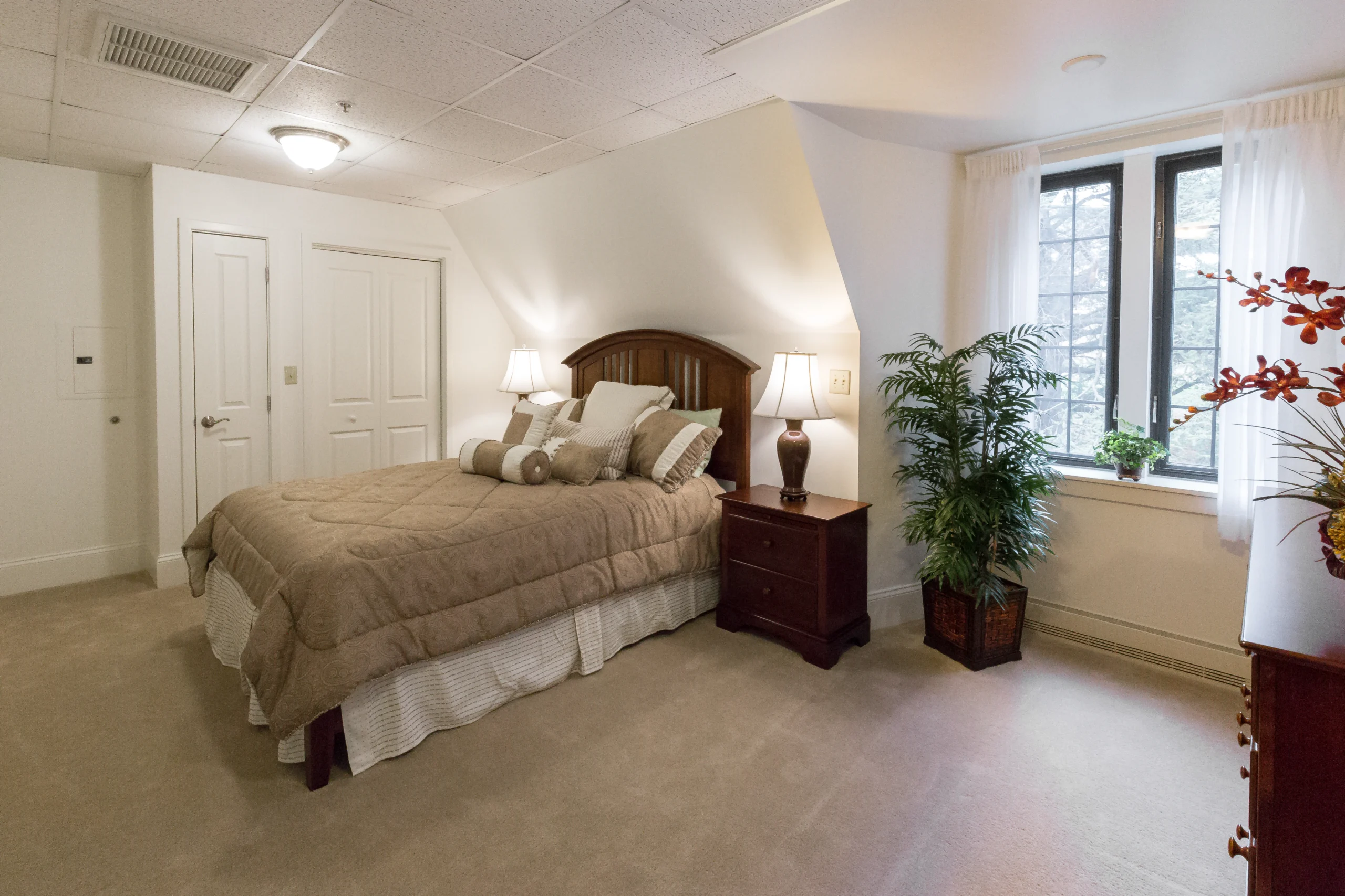 Neutral-toned bedroom with beige carpet, and deep wood furniture, including a bed, night stand and dresser.