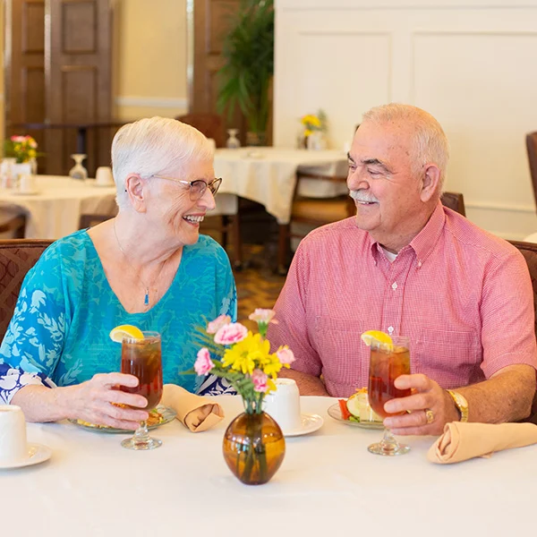 clubhouse Smiling senior couple seated in a dining room together while holding iced tea glasses.