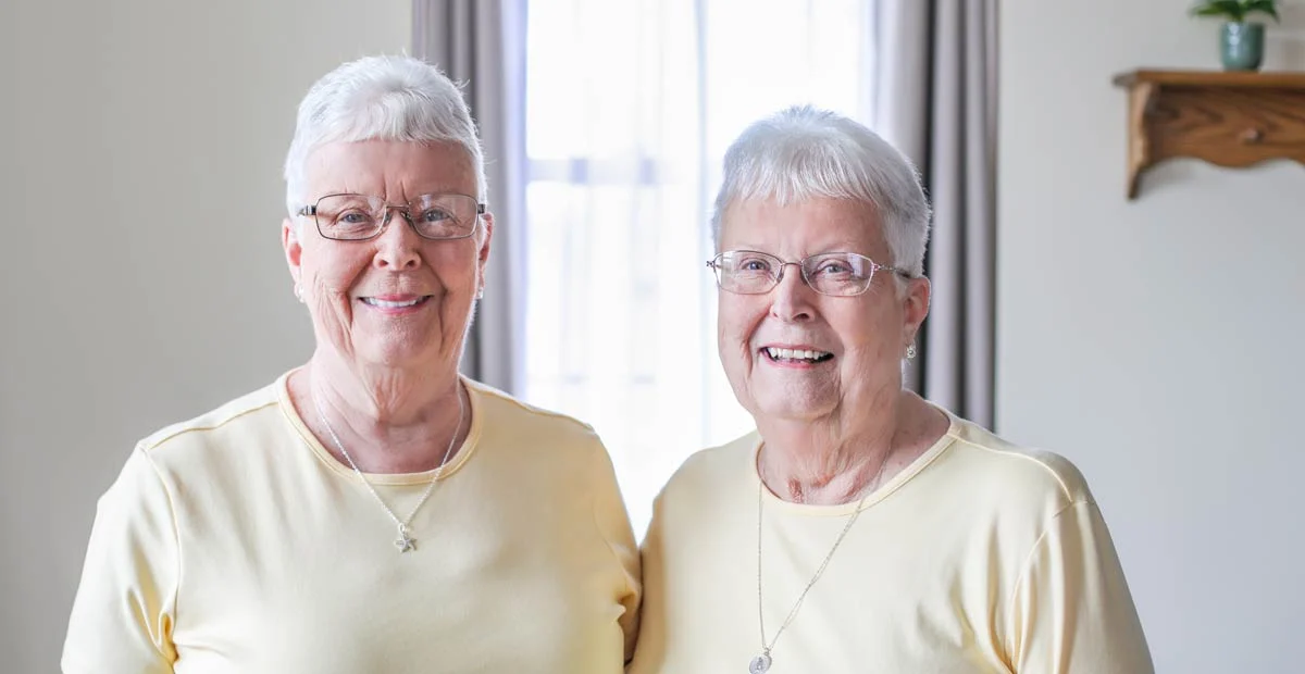 Kitty and Lois, smiling senior women with glasses in matching yellow shirts.
