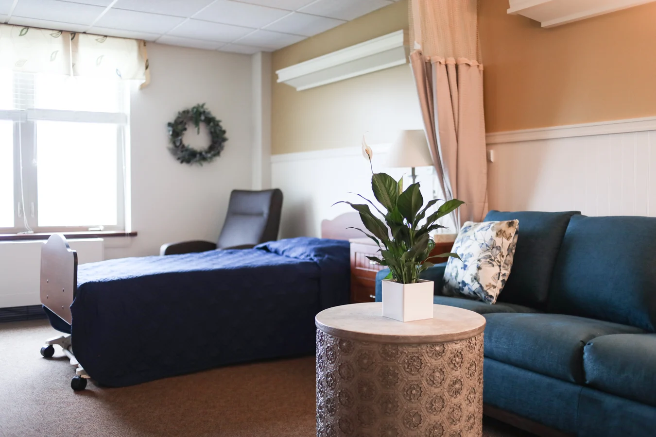 Evergreen Room, a cozy room with a bed, couch and tables. The bedspread and couch are blue and a wreathe hangs on the wall.