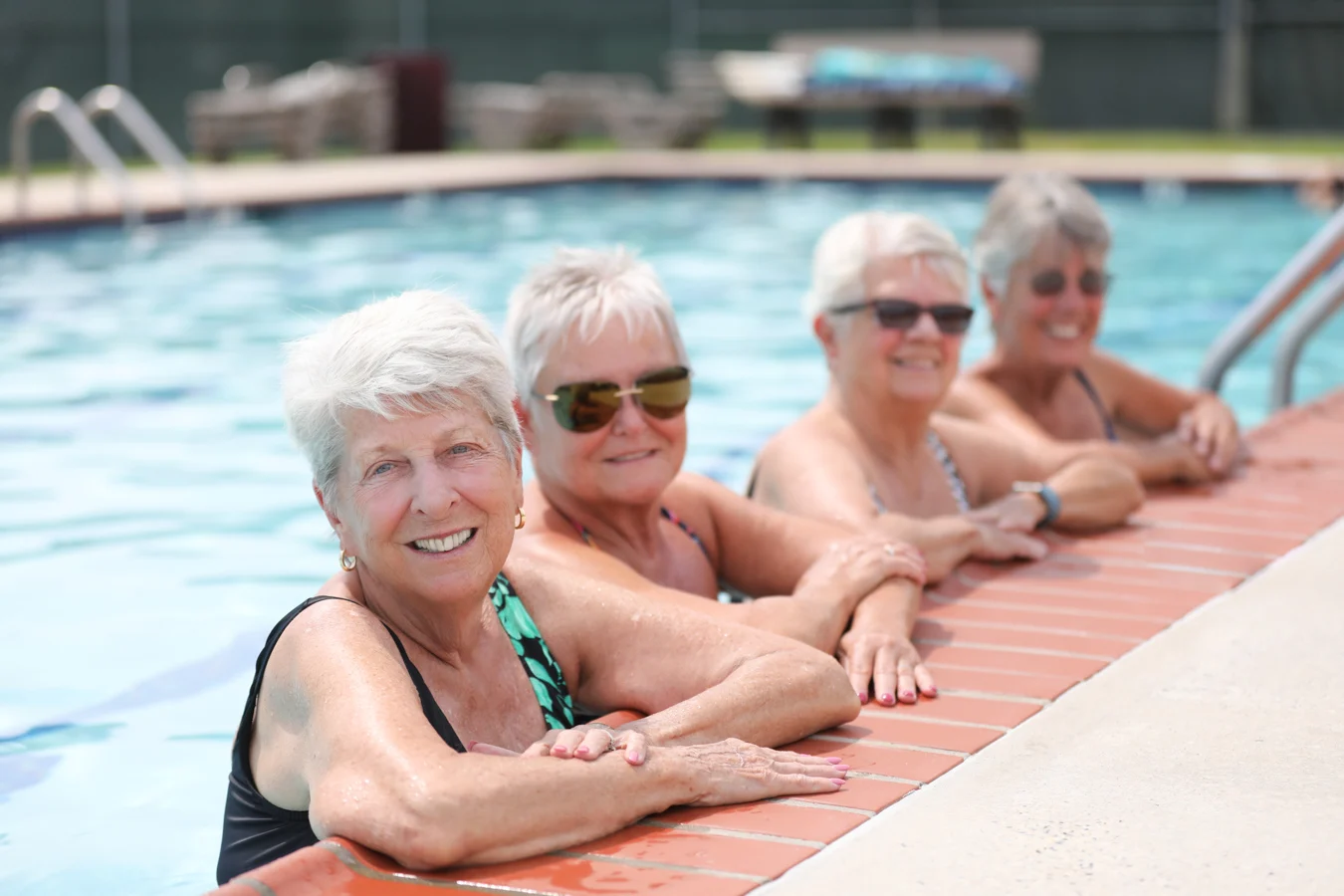 Group of smiling women at edge of a pool.