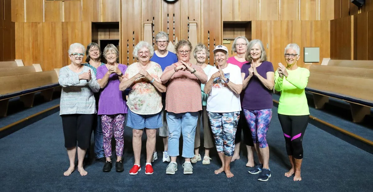 Tai Chi Club members standing together indoors with their hands brought together.