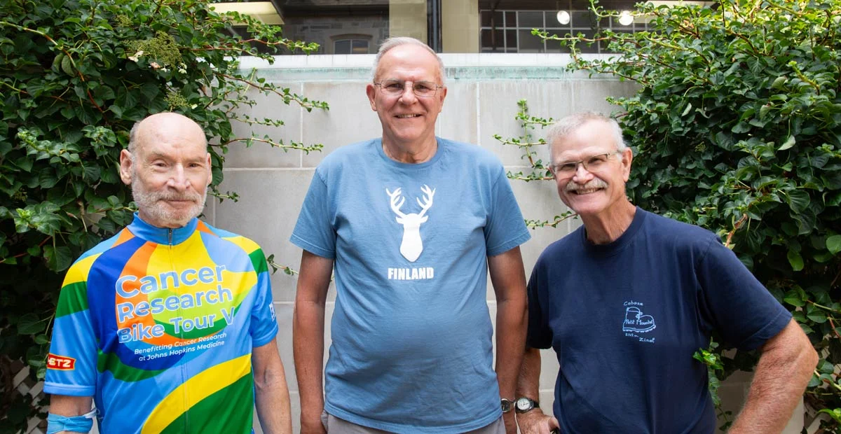 Three smiling senior men standing together outdoors.