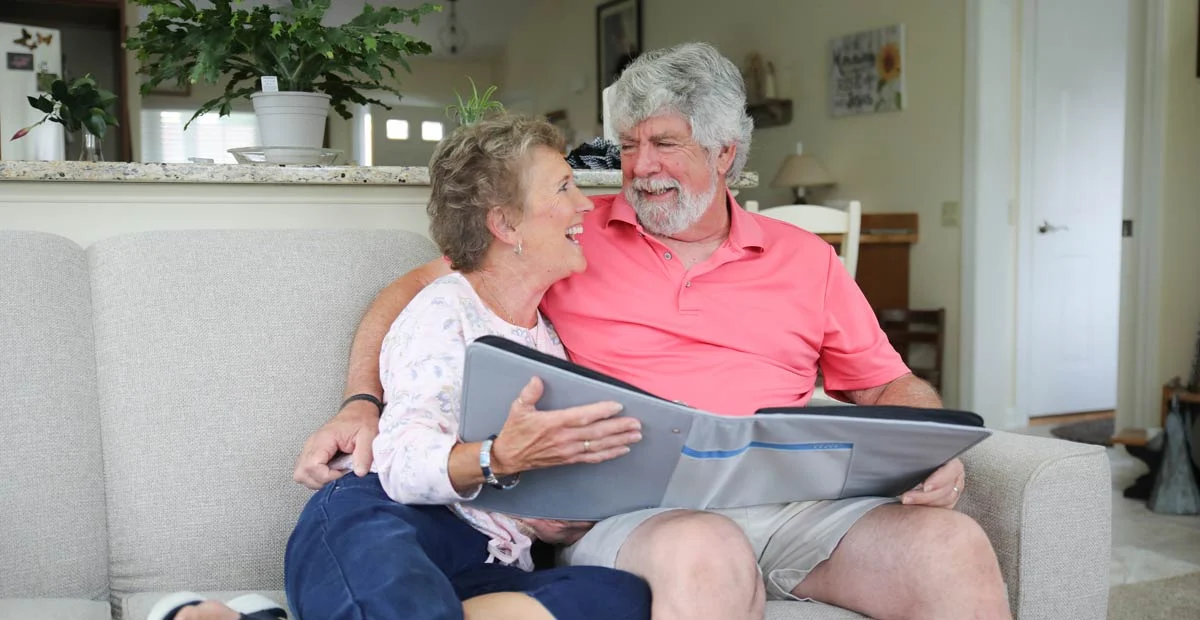 Vaughn and Debbie Nissley, a smiling senior couple on their couch together with a large book open in front of them.