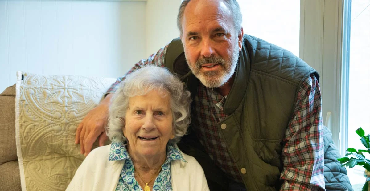 Alverna and Jeff Hoachlander, a smiling mature man and senior woman. Jeff is standing behind Alverna, who is seated.