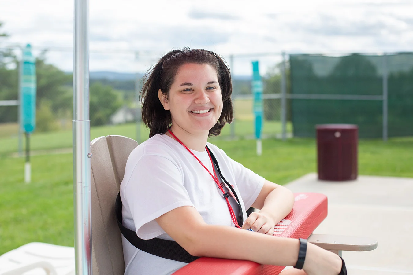 Smiling young woman sitting in lifeguard chair while holding a floatation device.