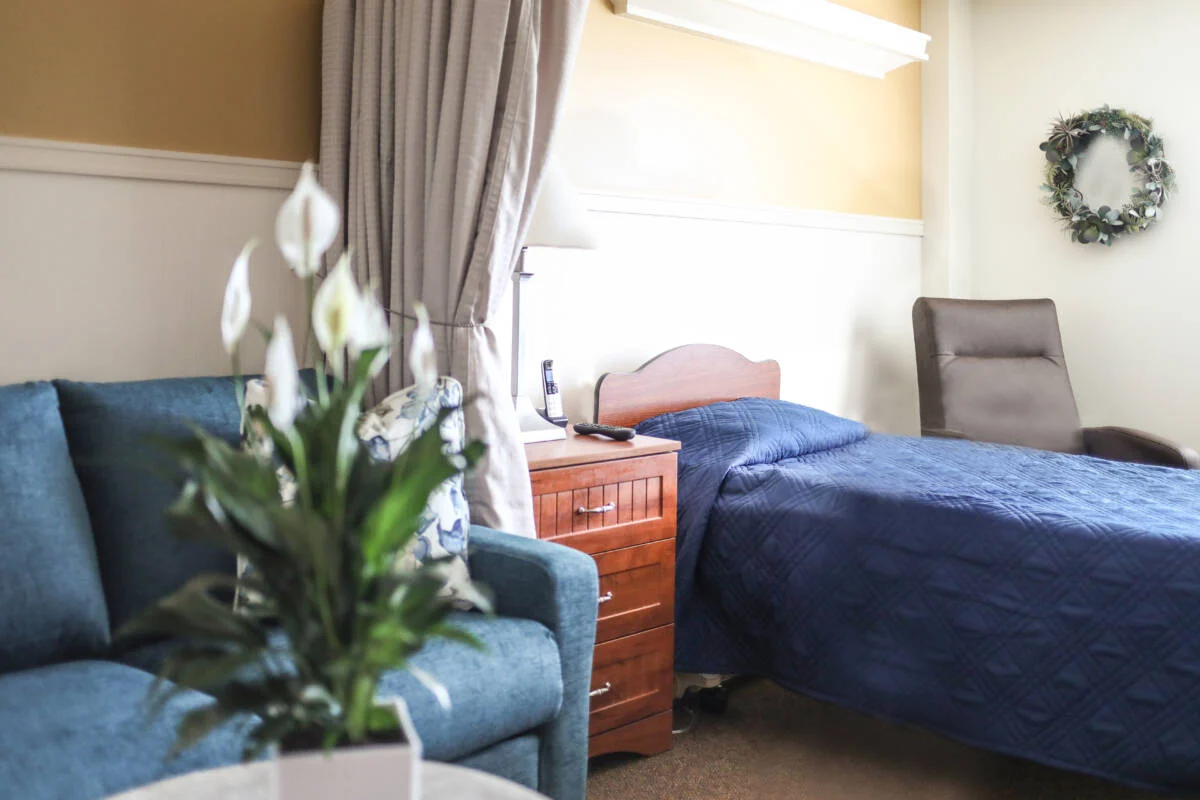 Interior of Evergreen room with a bed and couch, the couch and bed spread are blue and a wreath hangs on the wall behind the bed.