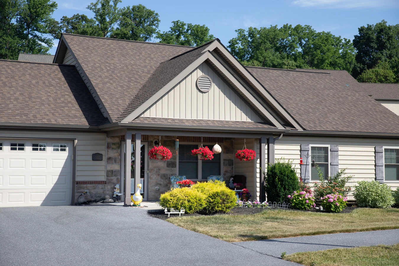 Front porch of a one-story cottage with a garden in the front lawn and flower baskets hanging from the porch.