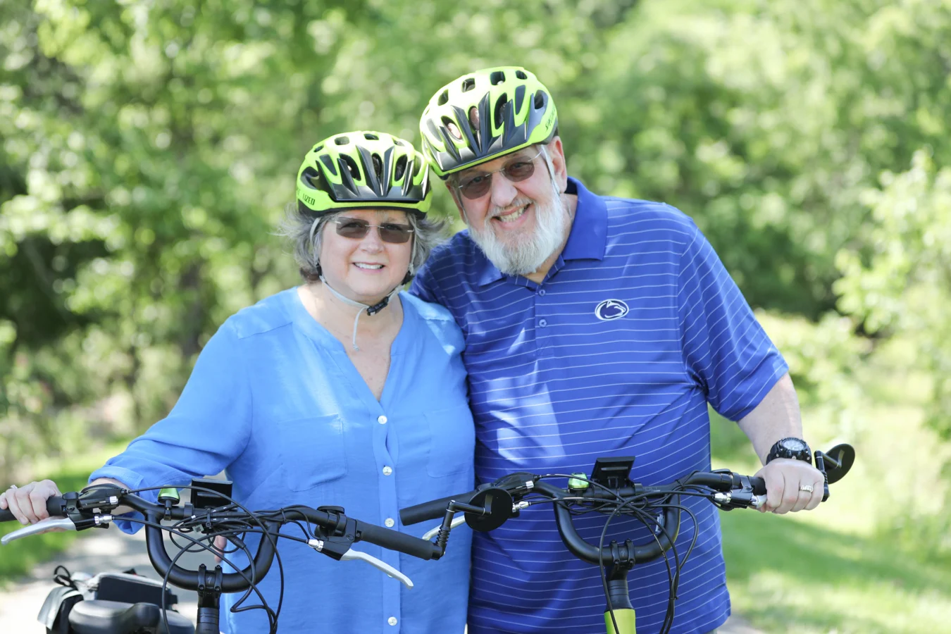 Smiling couple wearing sunglasses and helmets with their bikes outdoors.