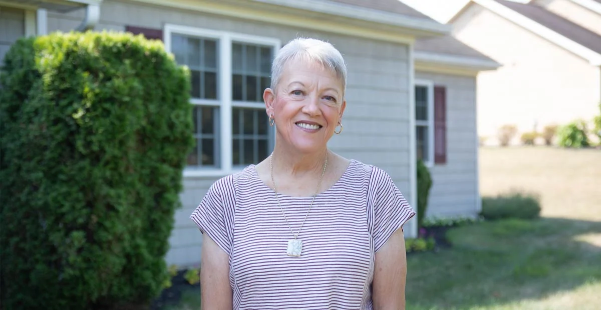 Smiling senior woman standing outdoors in front of her home.