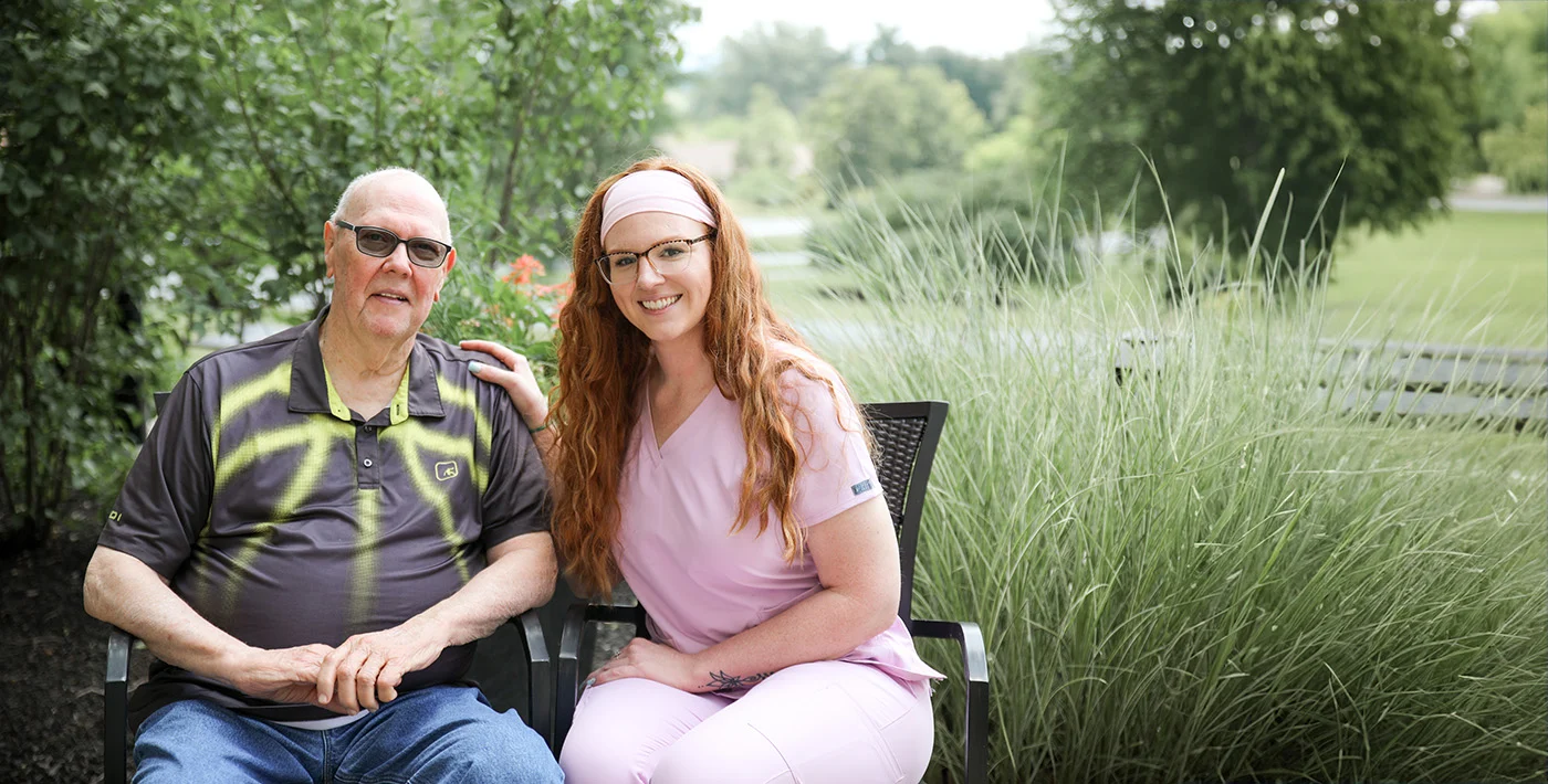 Smiling senior man sitting with nurse outdoors in patio chairs.