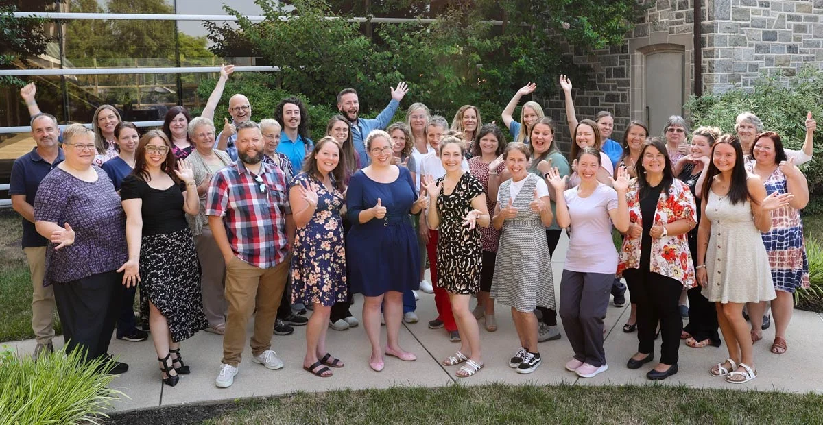 Group of staff in business attire standing outdoors together and celebrating.