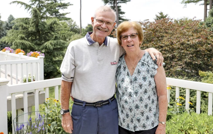 Chris and Becky Dunlap, a smiling senior couple standing on their patio.
