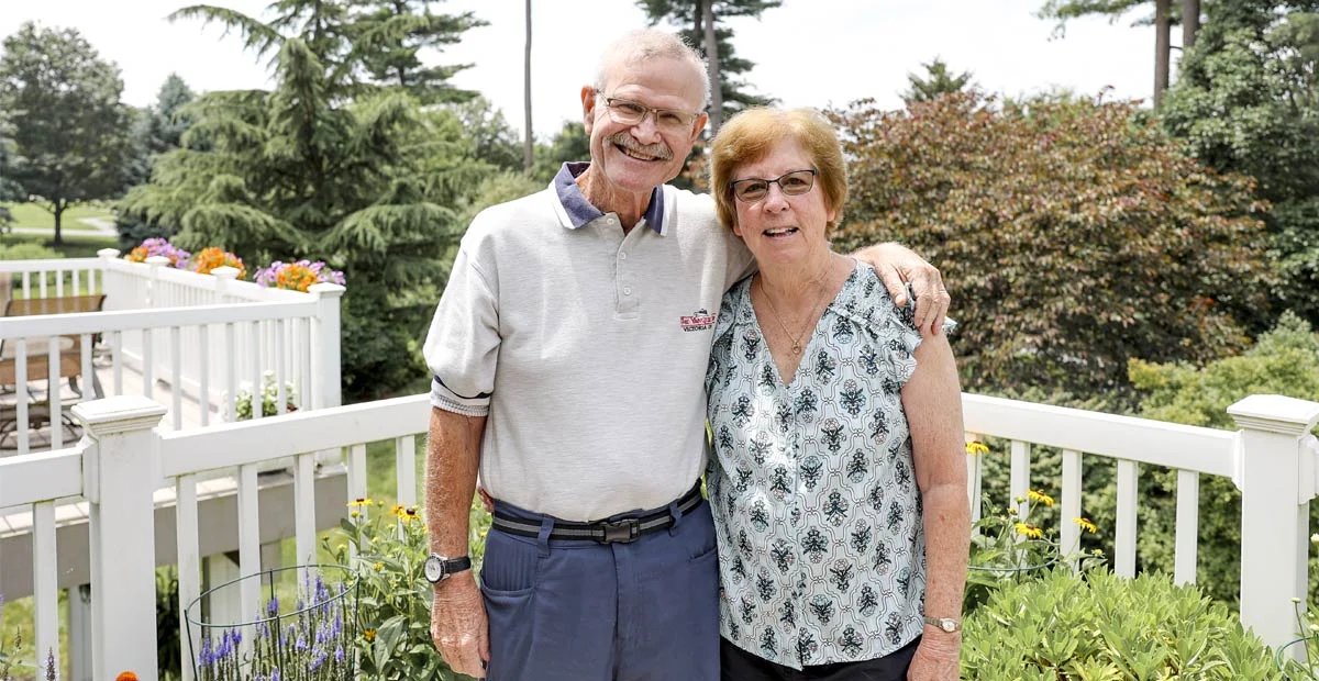 Chris and Becky Dunlap, a smiling senior couple standing on their patio.