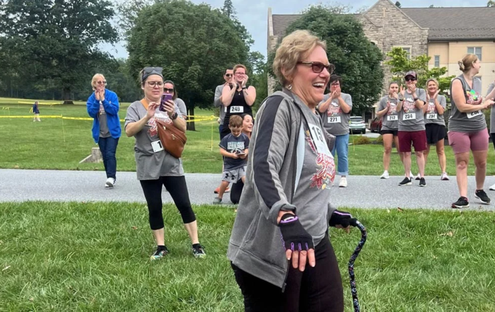 Maureen Jackson, a smiling senior woman walking with cane while crowd applauds behind her.