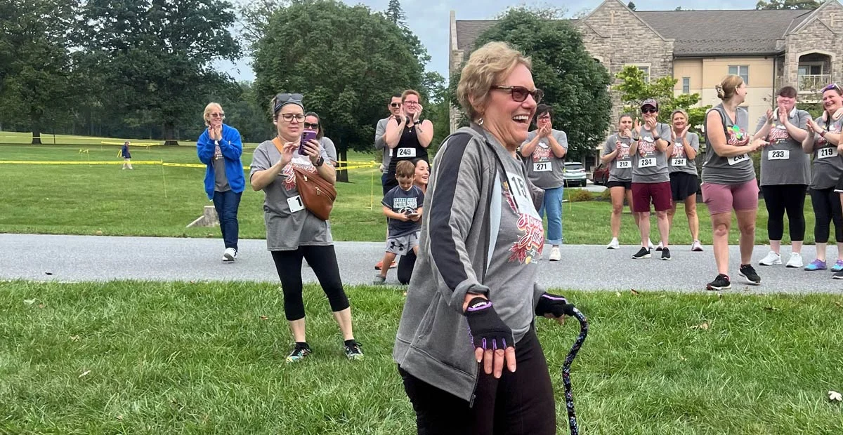Maureen Jackson, a smiling senior woman walking with cane while crowd applauds behind her.