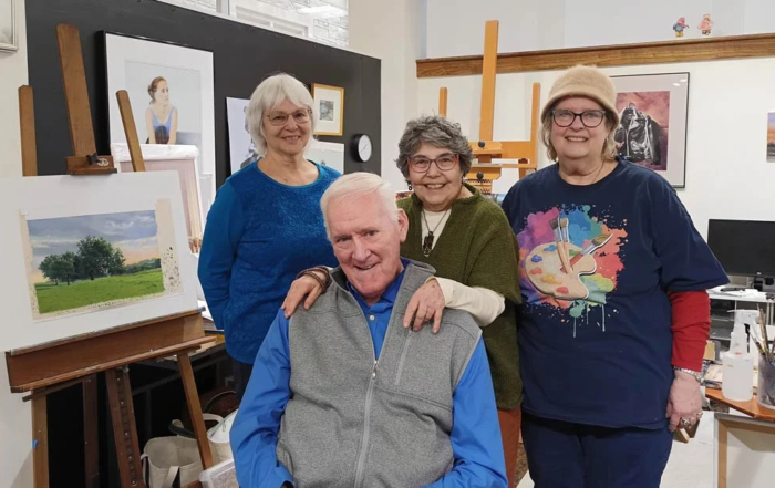 Group of smiling seniors in front of hanging artwork.