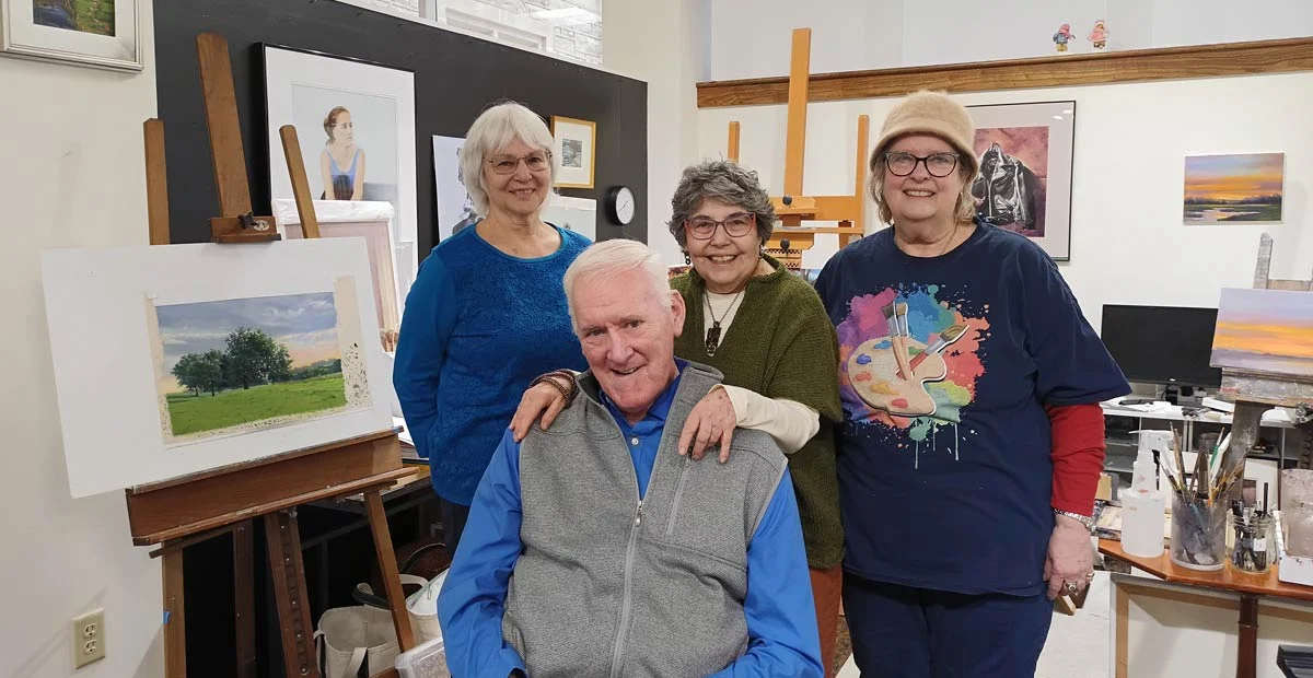 Group of smiling seniors in front of hanging artwork.