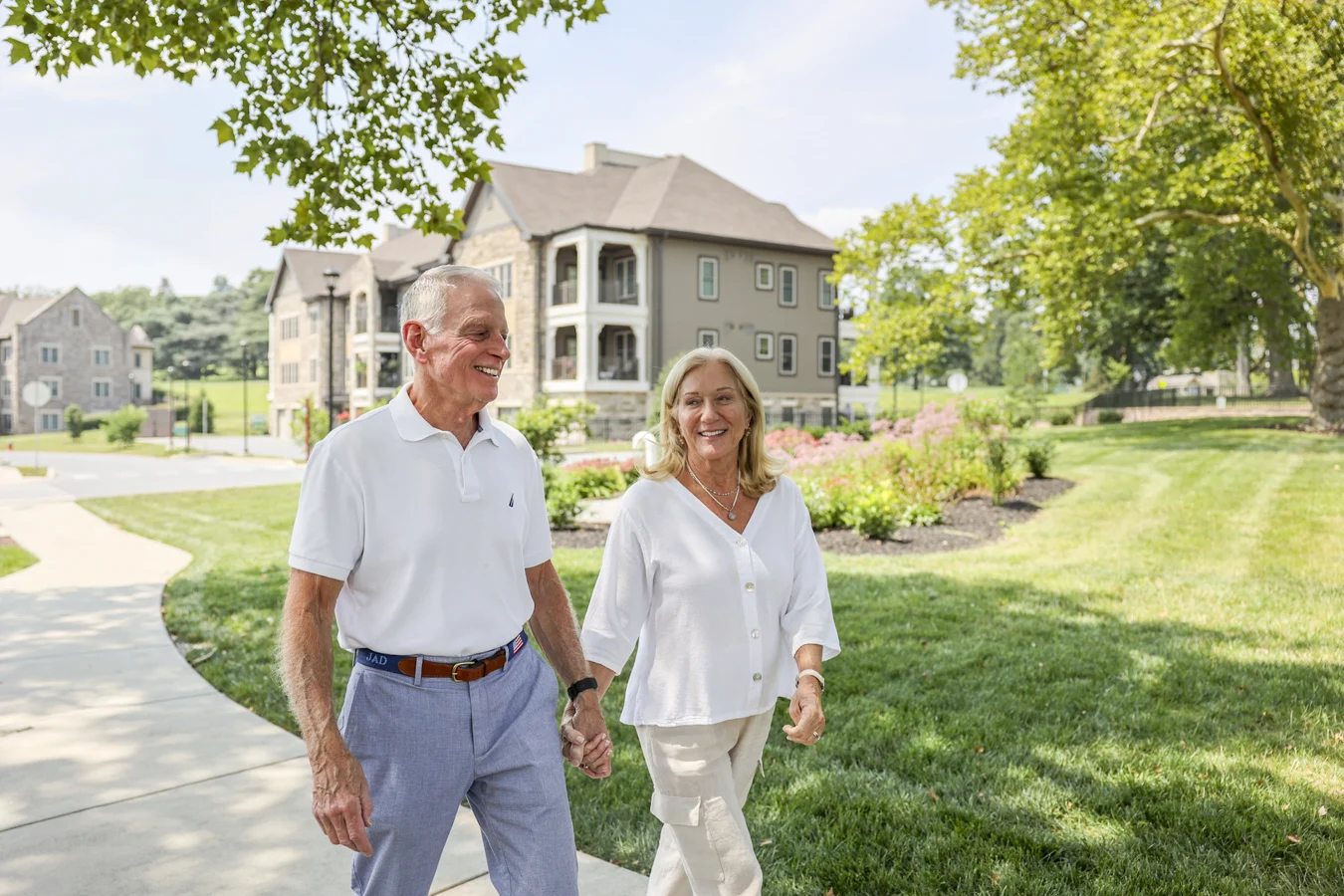 Smiling senior couple holding hands as they walk in front of a townhome building.