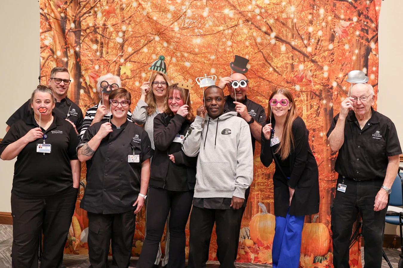 Smiling group of staff standing together with silly props in front of an autumn backdrop.