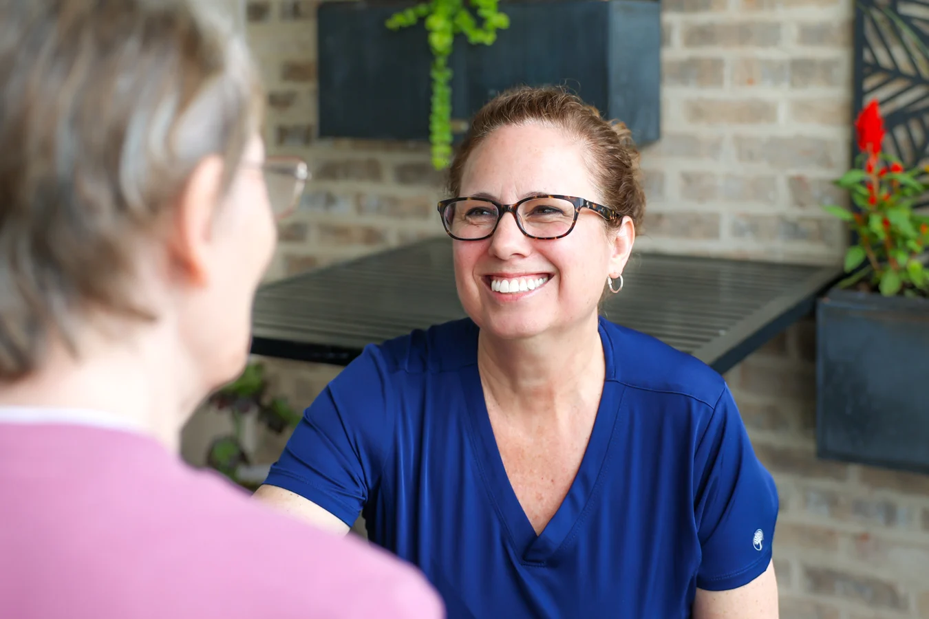 1W8A7756 Smiling nurse leaning down to speak to senior woman outdoors.