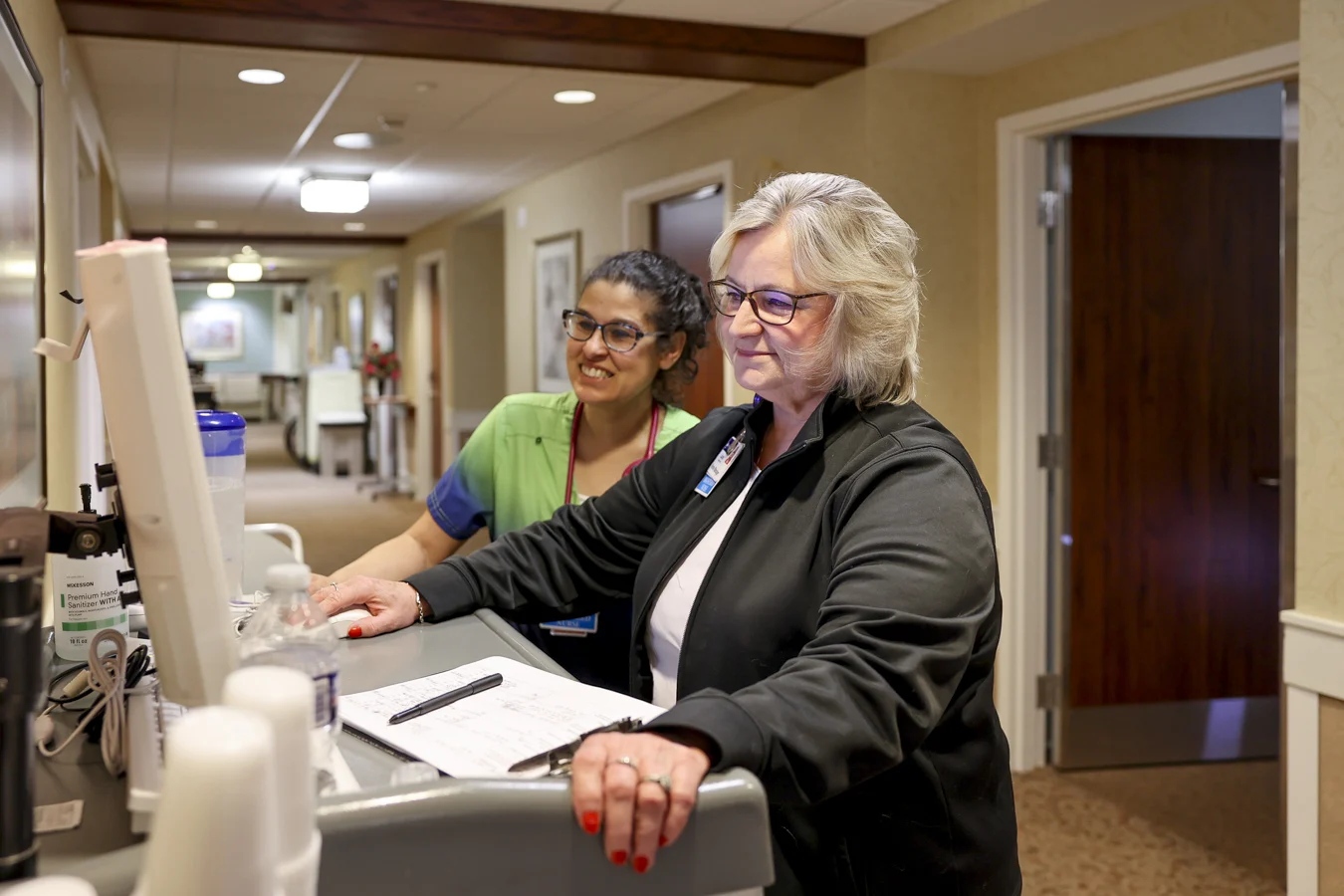 Smiling nurses in hallway at a computer station.