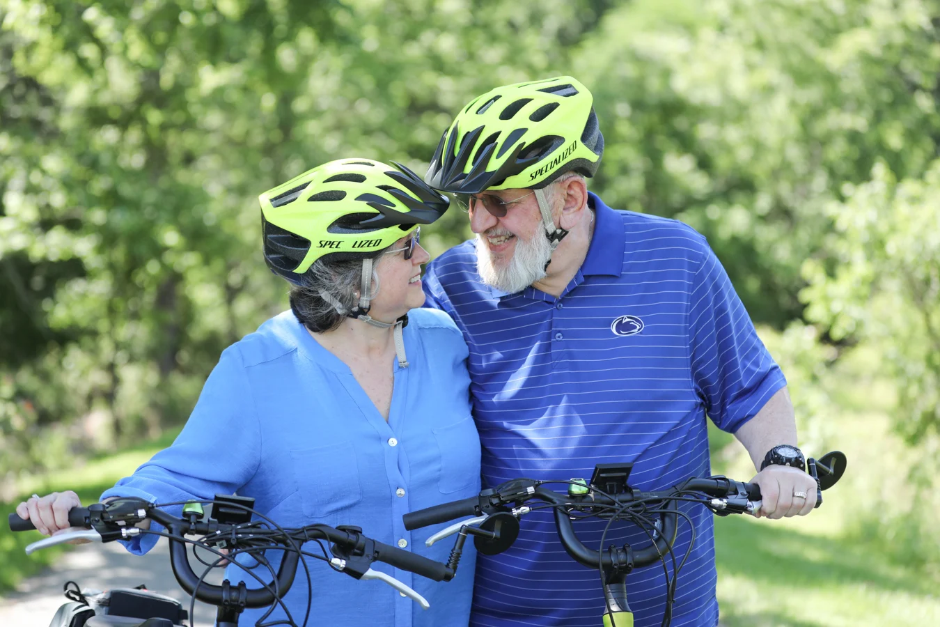 2V9A5670 Couple smiling while looking at one another as they walk with their bikes outdoors.