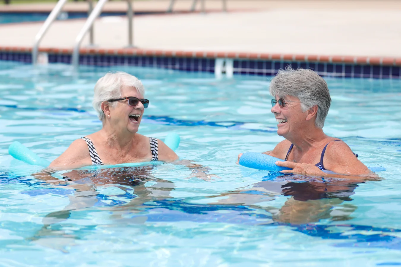 Two smiling women laughing while floating in a pool together.