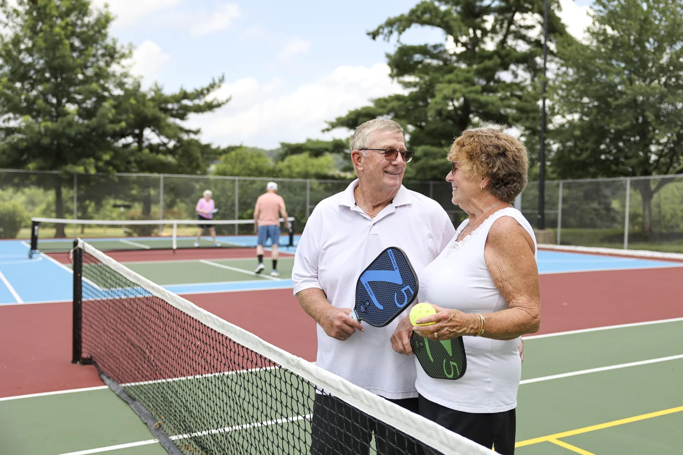 Smiling man and woman holding pickleball rackets while standing in court together.