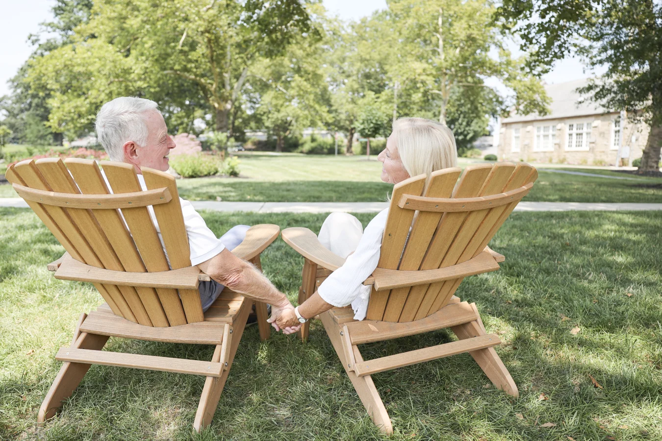 1W8A2297 Senior couple holding hands while seated in chairs outdoors.